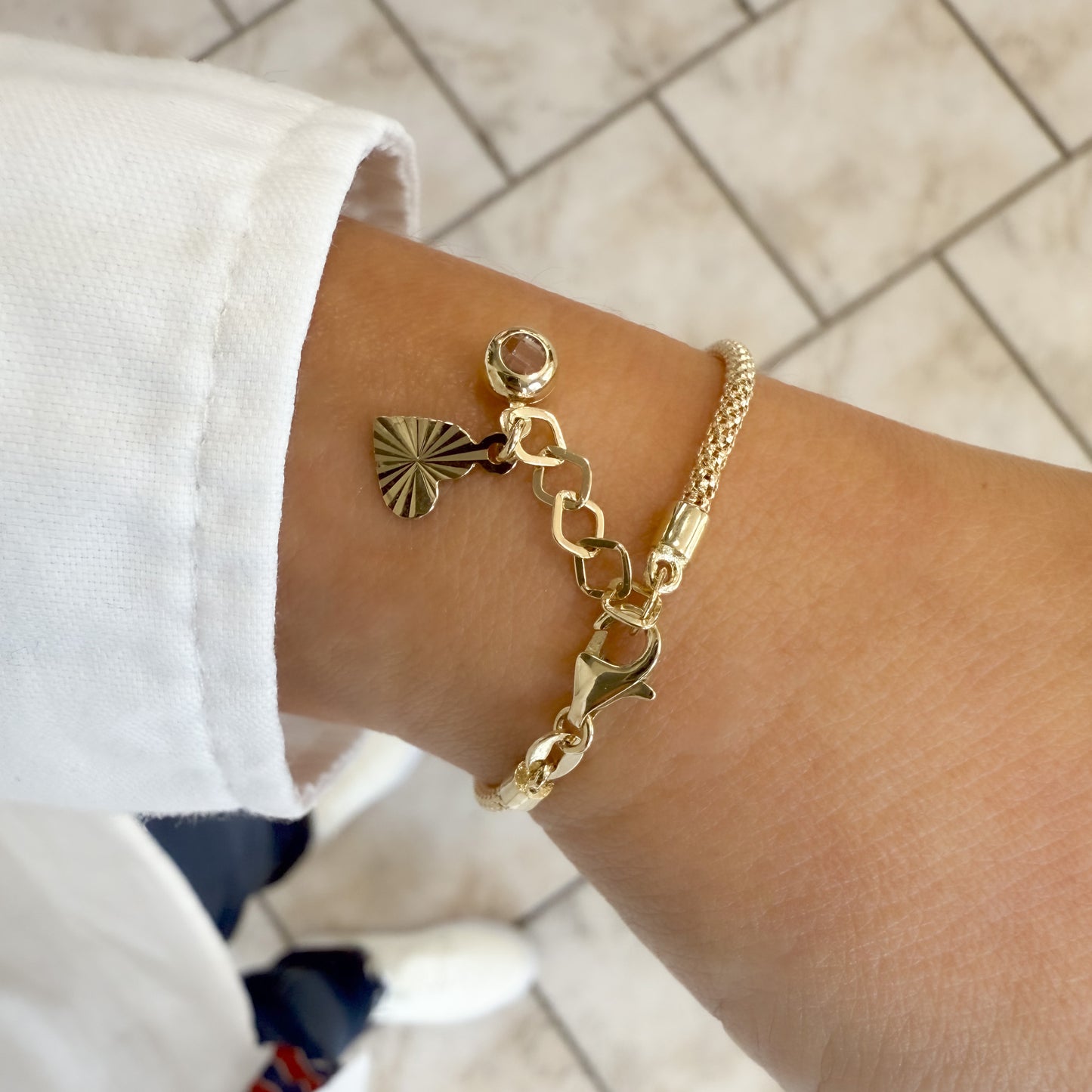Nahaufnahhme des Karabinerverschlusses des Schmetterling- Armbands, das zarte Verlängerungskettchen mit herzförmigem Anhänger und funkelnden Zirkonia-Stein, elegant am Handgelenk getragen.