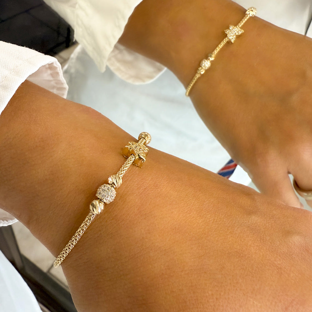 Seitliche Ansicht eines stilvollen Goldarmbands (585/14 Karat) am Handgelenk, mit Schmetterlingsmotiv in der Mitte, Pave-Kugeln und funkelnden Zirkonia, die sich in der glänzenden Oberfläche widerspiegeln.